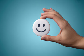 Optimistic Outlook Hand Holding Smiley Face Button Against a Serene Blue Backdrop Symbolizing Positivity