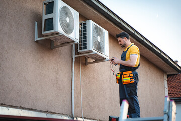 Technician installing an air conditioner on the wall of a house