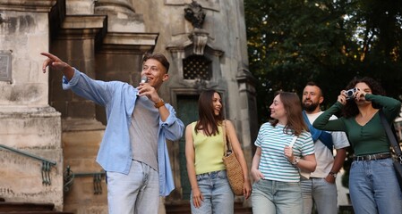 Guide with microphone and group of tourists on city street during excursion