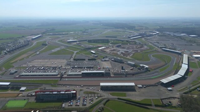 Aerial view of the sprawling Silverstone Circuit, a tapestry of asphalt and green fields under a hazy sky, Silverstone, United Kingdom.
