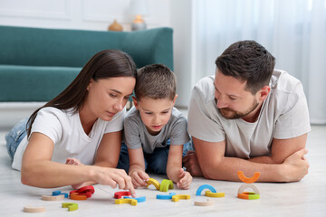 Parents and their son playing with toys on warm floor at home. Heating system