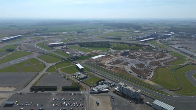 Aerial view of the iconic Silverstone Circuit, a tapestry of asphalt and green, contrasts sharply with the bustling pit lane, Silverstone, United Kingdom.