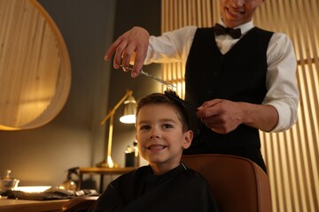 Professional barber cutting boy's hair in barbershop, closeup