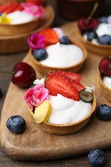 Sweet tartlets with berries and flowers on wooden table, closeup. Delicious dessert