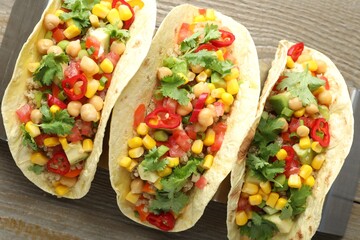 Tasty vegetarian tacos with chickpeas, corn and quinoa served on wooden table, top view