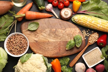 Healthy vegetarian food. Empty board surrounded by different products on dark textured table, flat lay