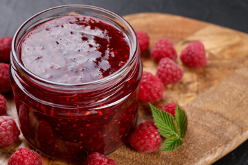 Sweet raspberry jam in glass jar and berries on table, closeup