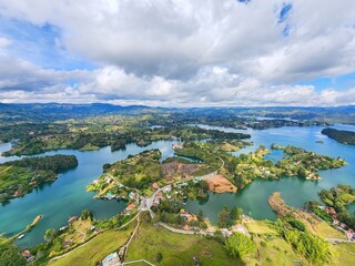 Fototapeta premium Aerial view revealing guatape's colorful landscape, featuring turquoise reservoir, verdant terrain, and rugged mountain silhouettes against dramatic colombian scenery