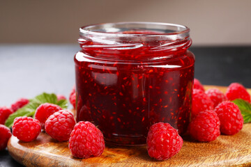 Sweet raspberry jam in glass jar and berries on table, closeup