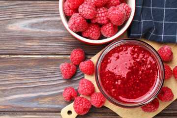 Sweet raspberry jam in glass jar and berries on wooden table, flat lay. Space for text
