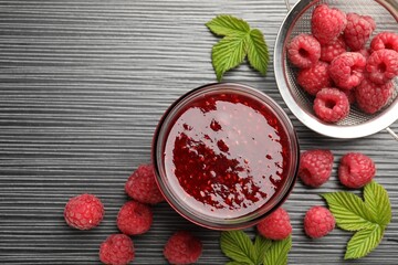 Sweet raspberry jam in glass jar and berries on dark gray wooden table, flat lay. Space for text