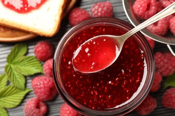 Taking sweet raspberry jam with spoon from glass jar on table, top view