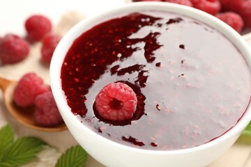 Sweet raspberry jam in bowl and berries on table, closeup
