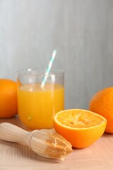 Fresh orange juice in glass, fruits and juicer on wooden table, closeup