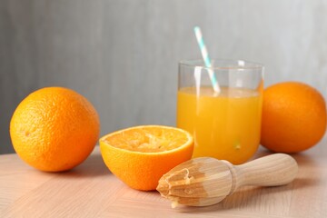 Fresh orange juice in glass, fruits and juicer on wooden table, closeup