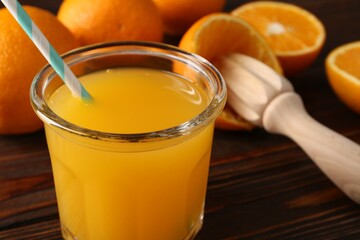 Fresh orange juice in glass, fruits and juicer on wooden table, closeup