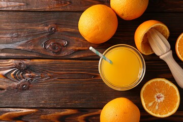 Fresh orange juice in glass, fruits and juicer on wooden table, flat lay. Space for text