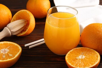 Fresh orange juice in glass, fruits, straws and juicer on wooden table, closeup