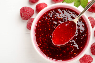 Sweet raspberry jam in bowl, berries and green leaves on white table, flat lay. Space for text
