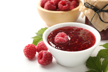 Sweet raspberry jam, berries and green leaves on white wooden table, closeup. Space for text