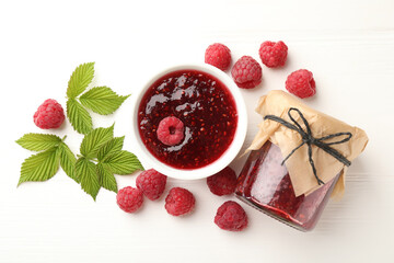 Sweet raspberry jam, berries and green leaves on white wooden table, flat lay