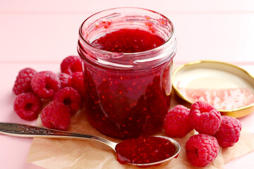 Sweet raspberry jam in glass jar and berries on table, closeup