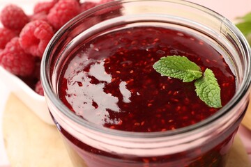 Sweet raspberry jam in glass jar, berries and mint on table, closeup