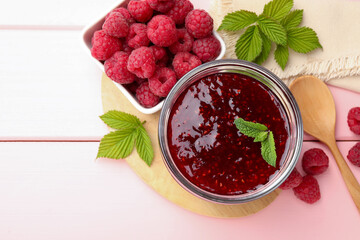 Sweet raspberry jam in glass jar, berries and mint on pink wooden table, flat lay