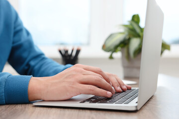 Copywriter using laptop at wooden table indoors, closeup