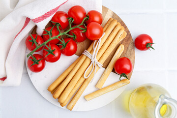 Delicious grissini sticks with fresh tomatoes and oil on white tiled table, flat lay