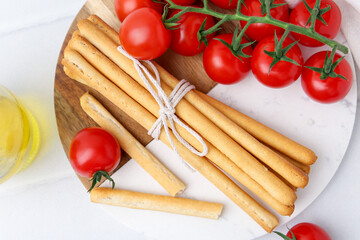 Delicious grissini sticks with fresh tomatoes on white table, flat lay