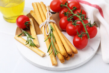 Delicious grissini sticks, rosemary and fresh tomatoes on white table, closeup