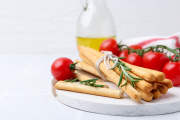 Delicious grissini sticks, rosemary and fresh tomatoes on white table, closeup. Space for text