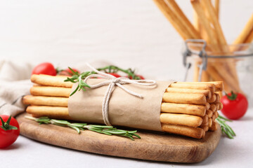 Delicious grissini sticks, rosemary and fresh tomatoes on light table, closeup