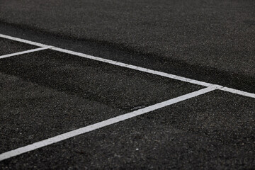 White painted lines intersecting on dark asphalt pavement creating geometric corner marking pattern