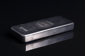 Old and scratched silver bar, side view, on black glass. Stamped and numbered cast silver ingot, of one kilogram, about 32 troy oz of metal, with a purity of 999.0, that is 99.9 percent pure silver.