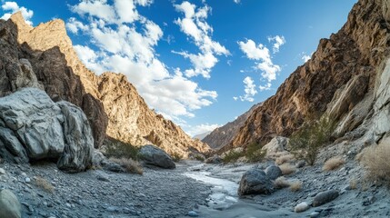 Rocky gorge with a clear stream bed under a partly cloudy sky.