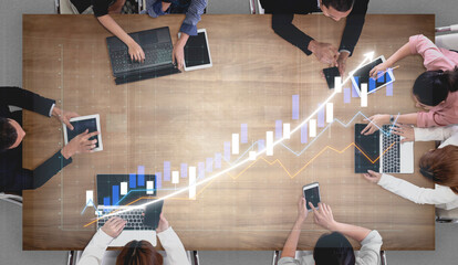 Aerial view of a collaborative business meeting where diverse professionals analyze financial data on laptops and tablets with growth charts displayed. Impute