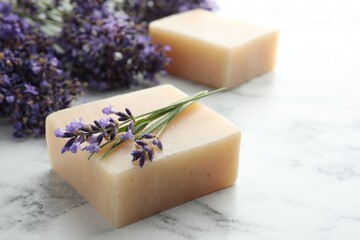 Soap bars and lavender flowers on white marble table, closeup. Space for text