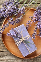 Aromatic soap bar and lavender flowers on wooden table, flat lay
