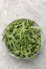 Fresh ripe green arugula leaves in bowl on grey table, top view