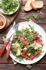 Tasty salad with arugula and prosciutto served on wooden table, flat lay