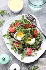 Tasty salad with arugula, vegetables and egg served on grey table, flat lay