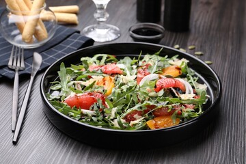 Tasty salad with arugula, cheese, grapefruit, vegetable and balsamic sauce on dark wooden table, closeup