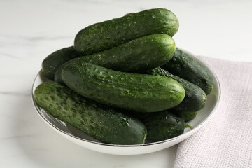 Fresh cucumbers in bowl on white marble table, closeup