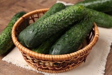 Fresh cucumbers in wicker basket on wooden table, closeup