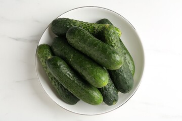 Fresh cucumbers in bowl on white marble table, top view
