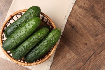 Fresh cucumbers in wicker basket on wooden table, top view