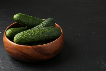 Fresh cucumbers in bowl on dark textured table, closeup. Space for text