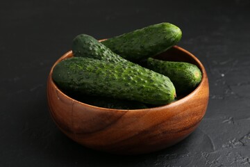 Fresh cucumbers in bowl on dark textured table, closeup